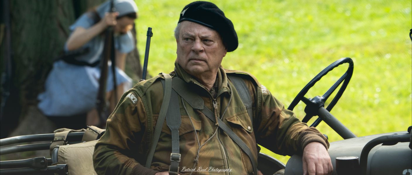 A striking image of an old commander sitting on a jeep, his face marked by years of experience. His stern gaze reflects authority and determination, capturing the weight of leadership in a moment of quiet intensity.